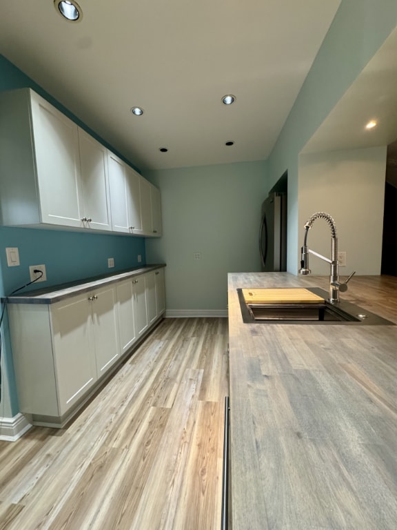 kitchen with white cabinetry, sink, refrigerator, and light hardwood / wood-style flooring