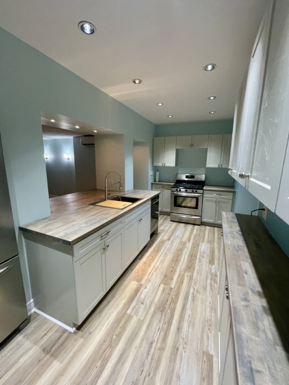 kitchen featuring wood counters, sink, gas range, light wood-type flooring, and black dishwasher