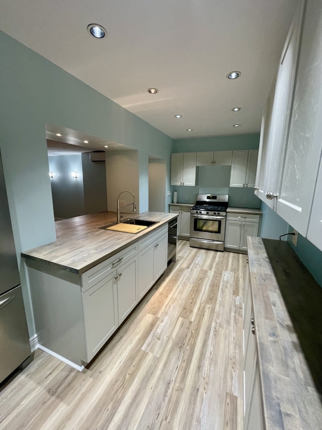 kitchen featuring black dishwasher, recessed lighting, light wood-style flooring, a sink, and gas range