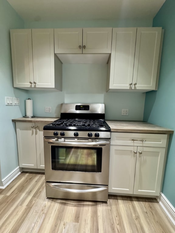 kitchen featuring stainless steel gas stove, white cabinetry, and light hardwood / wood-style floors