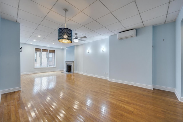 unfurnished living room featuring a drop ceiling, a wall mounted air conditioner, light hardwood / wood-style floors, and ceiling fan