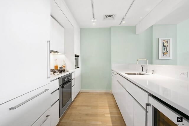 kitchen with stainless steel appliances, white cabinetry, sink, and wine cooler