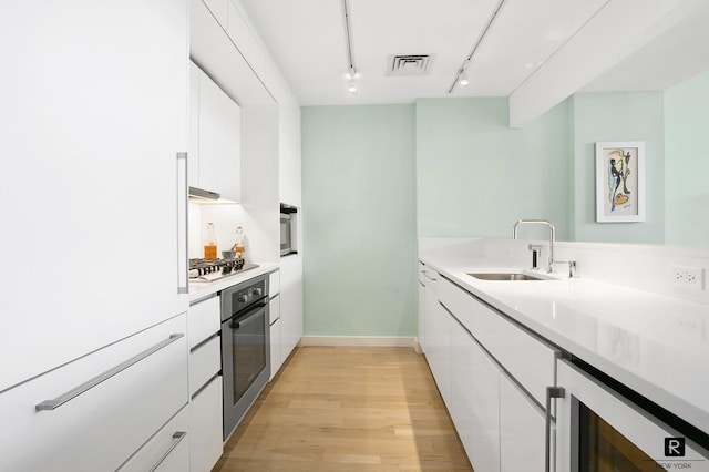 kitchen with beverage cooler, white cabinetry, stainless steel appliances, and a sink