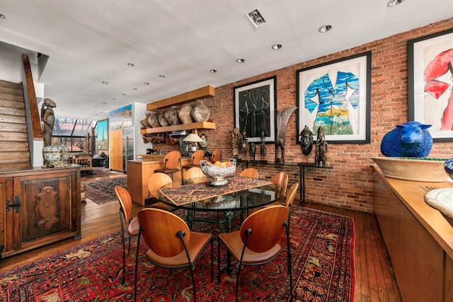 dining area with wood-type flooring and brick wall