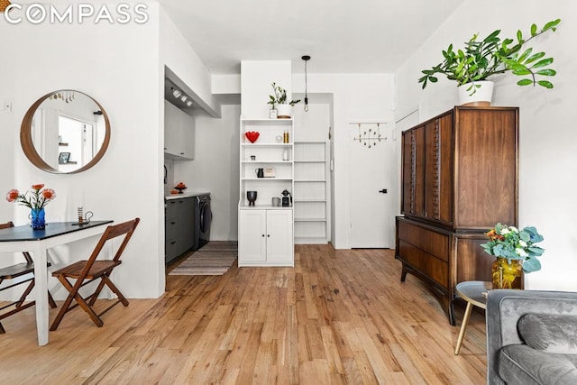 kitchen with decorative light fixtures, white cabinets, washer and dryer, and light wood-type flooring