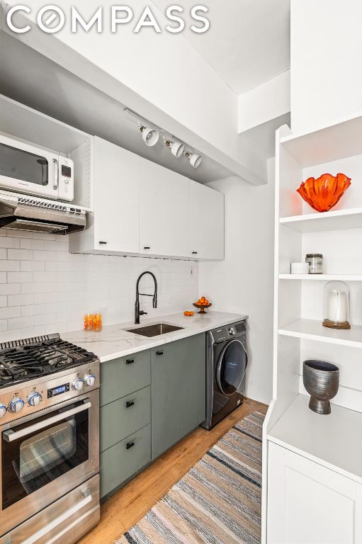 kitchen with washer / dryer, white cabinetry, extractor fan, gas range, and sink