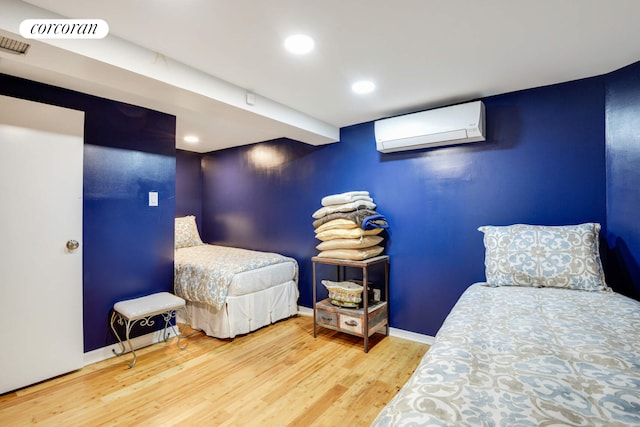 bedroom with a wall unit AC, recessed lighting, visible vents, wood finished floors, and baseboards