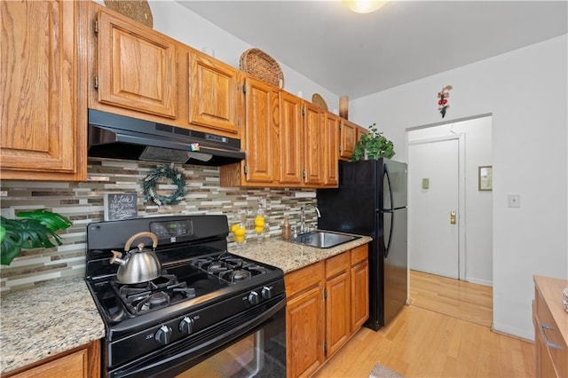 kitchen with a sink, black appliances, light wood-style floors, under cabinet range hood, and backsplash