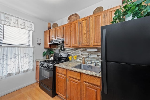 kitchen with a healthy amount of sunlight, a sink, black appliances, under cabinet range hood, and backsplash