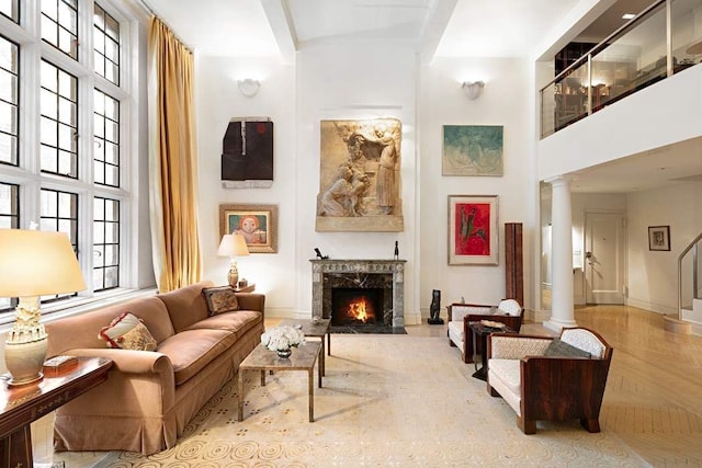 living area with decorative columns, a premium fireplace, light parquet floors, and a high ceiling