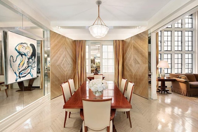 dining area featuring an inviting chandelier, ornamental molding, light parquet flooring, and wooden walls