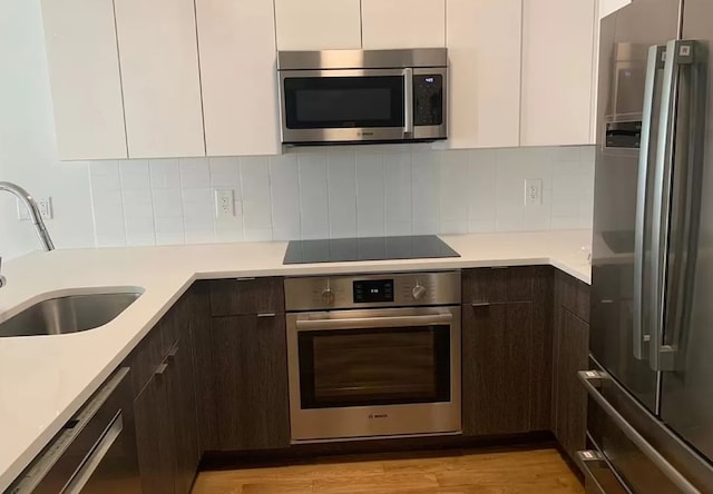 kitchen featuring white cabinetry, backsplash, dark brown cabinets, and black appliances