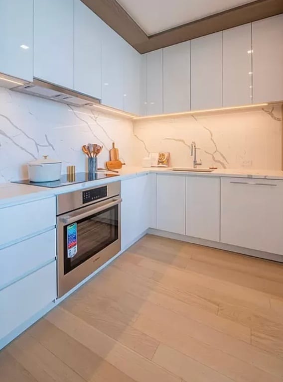 kitchen with sink, stainless steel oven, white cabinets, and light wood-type flooring