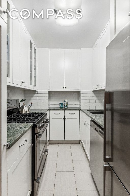 kitchen with white cabinetry, dark stone countertops, decorative backsplash, light tile patterned floors, and stainless steel appliances