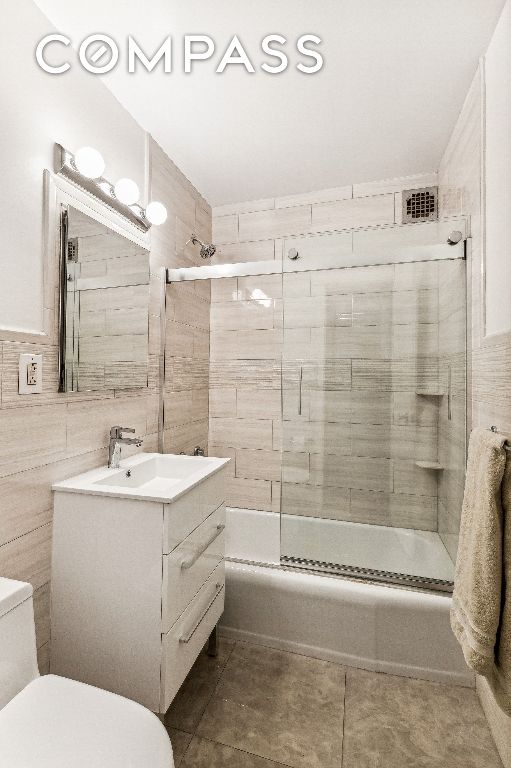 full bathroom featuring bath / shower combo with glass door, tile walls, tile patterned flooring, vanity, and toilet