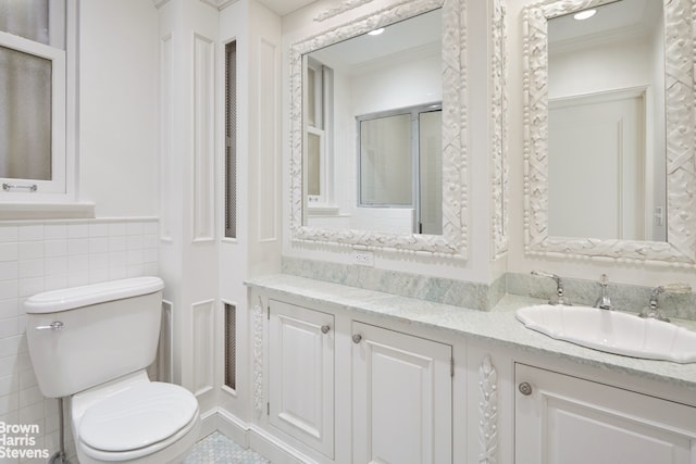 bathroom featuring toilet, crown molding, vanity, and a wainscoted wall