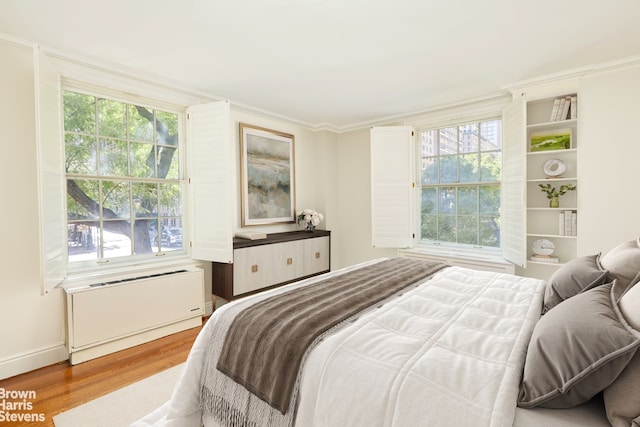 bedroom with crown molding, multiple windows, radiator heating unit, and wood finished floors