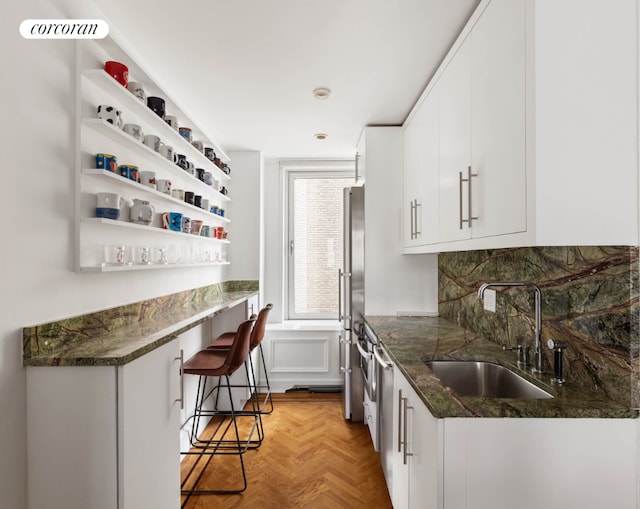 kitchen with stainless steel fridge, a breakfast bar area, light parquet flooring, white cabinets, and sink