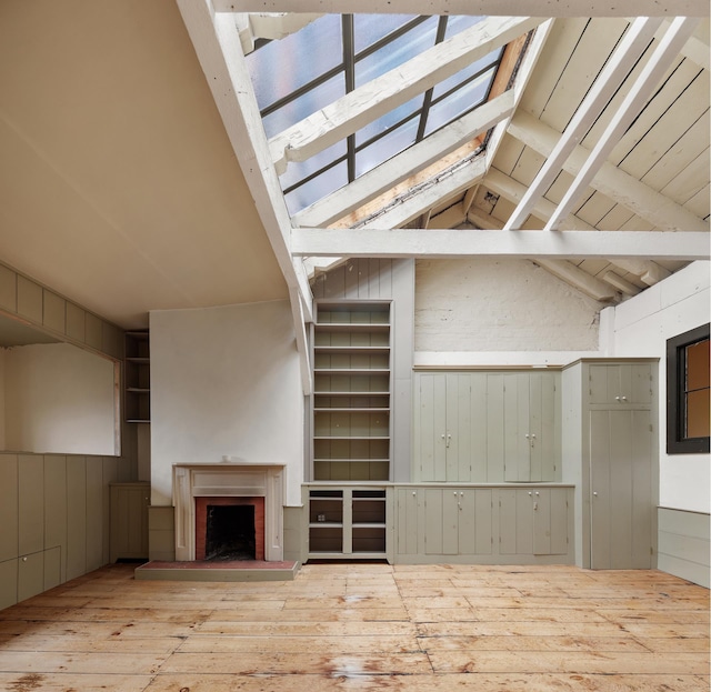 unfurnished living room with a brick fireplace, light wood-type flooring, lofted ceiling with beams, and wood walls