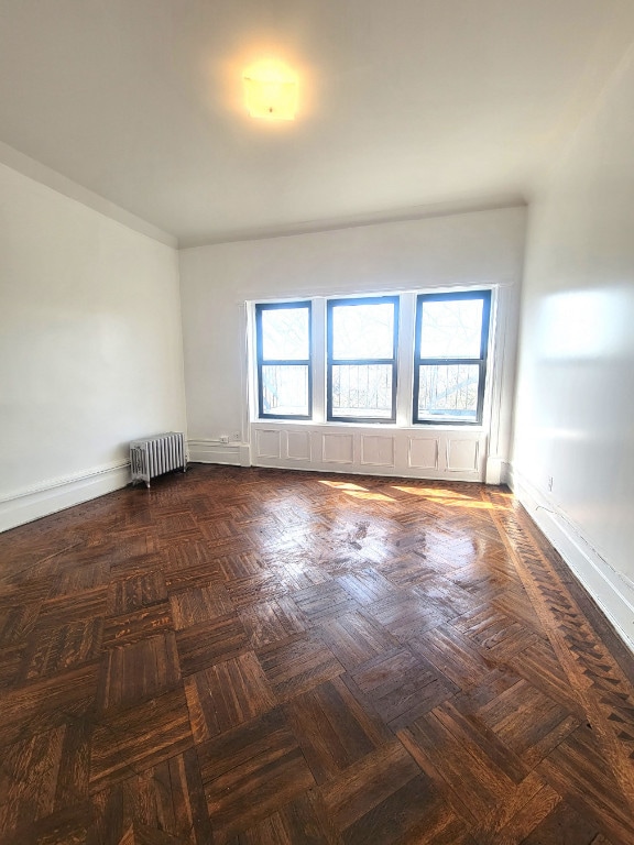 unfurnished room with dark parquet flooring and radiator heating unit