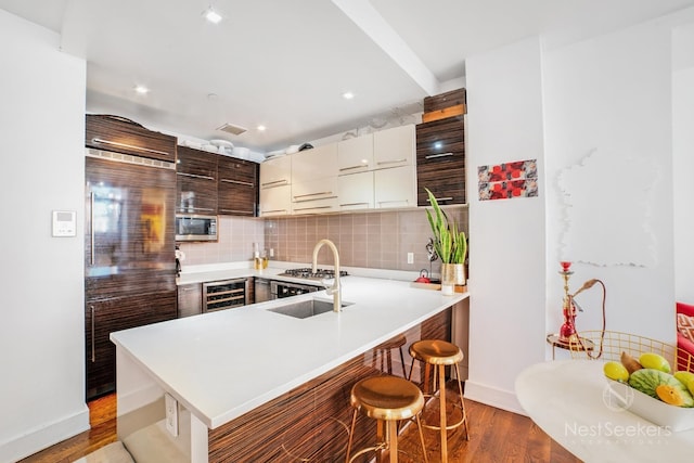 kitchen with dark brown cabinetry, a breakfast bar, sink, stainless steel microwave, and kitchen peninsula