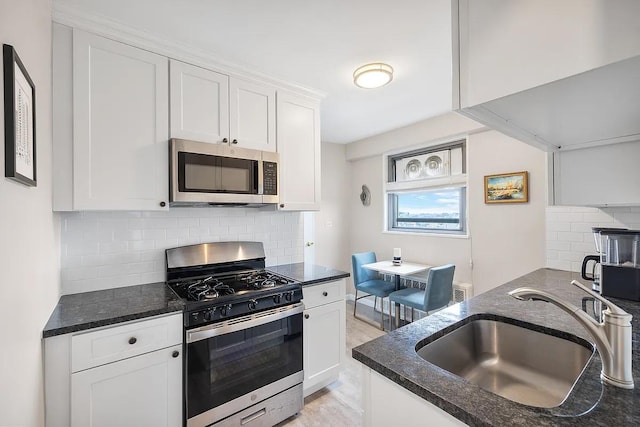 kitchen featuring dark stone counters, appliances with stainless steel finishes, a sink, and white cabinetry