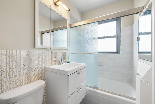 full bathroom with tile walls, bath / shower combo with glass door, toilet, and vanity