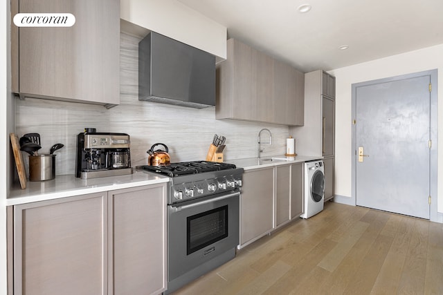 kitchen with washer / dryer, gas stove, gray cabinetry, a sink, and exhaust hood