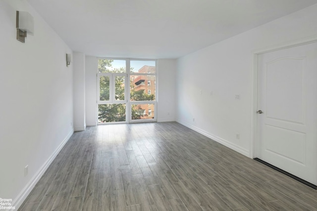 empty room featuring a wall of windows, wood finished floors, and baseboards