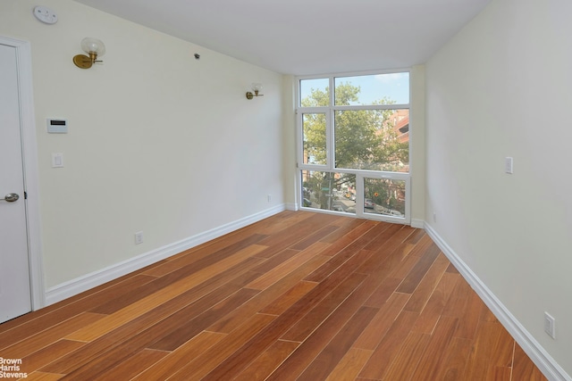 spare room with floor to ceiling windows, baseboards, and wood finished floors