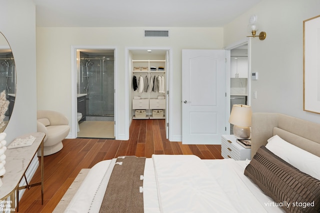 bedroom featuring a spacious closet, visible vents, connected bathroom, wood finished floors, and a closet