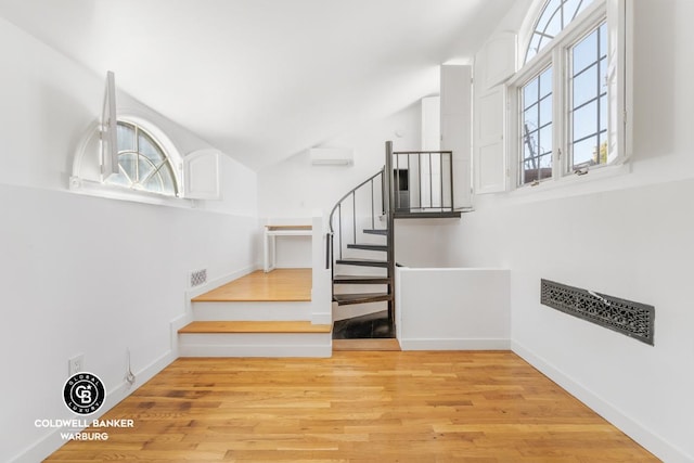 staircase featuring an AC wall unit, plenty of natural light, and hardwood / wood-style floors