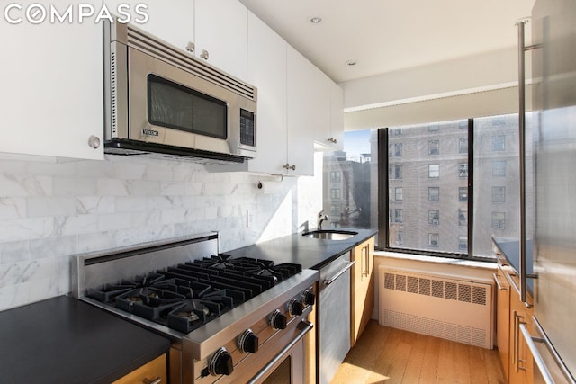 kitchen featuring appliances with stainless steel finishes, radiator, white cabinetry, sink, and light hardwood / wood-style flooring