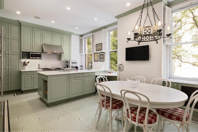 kitchen featuring decorative light fixtures, tasteful backsplash, sink, green cabinetry, and crown molding