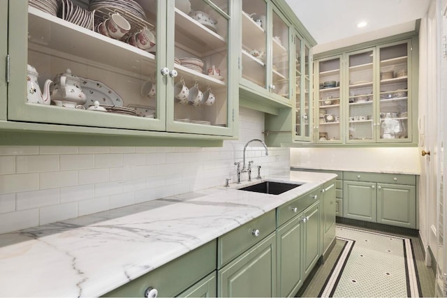 kitchen with green cabinets, light stone counters, tasteful backsplash, and sink