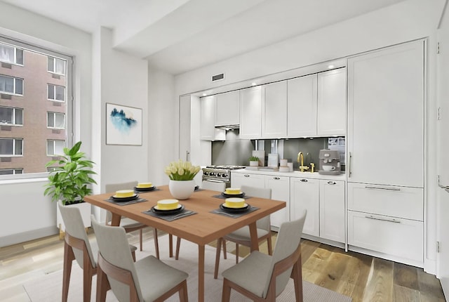 kitchen with decorative backsplash, sink, white cabinetry, light wood-type flooring, and stainless steel range