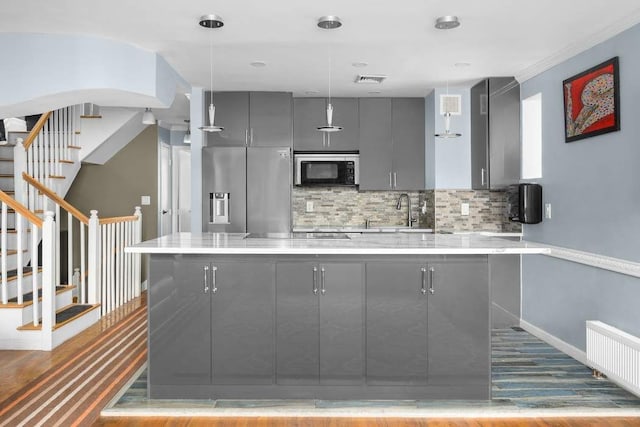 kitchen with hanging light fixtures, radiator heating unit, gray cabinets, stainless steel appliances, and backsplash