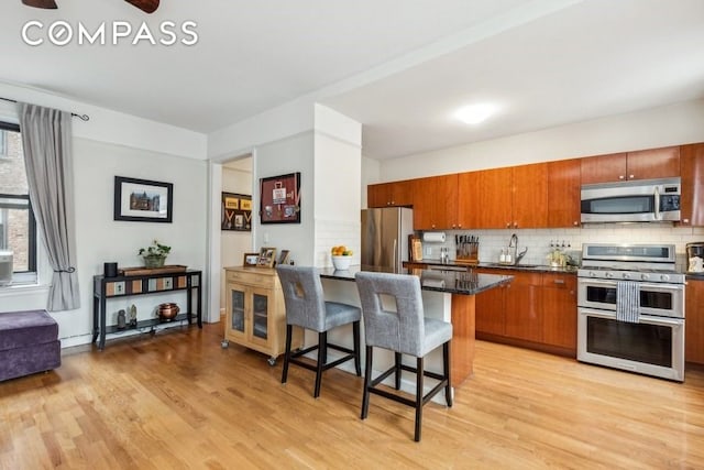 kitchen featuring tasteful backsplash, a breakfast bar area, stainless steel appliances, light wood-type flooring, and a sink