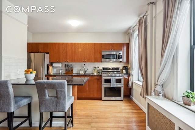 kitchen with light wood-style floors, appliances with stainless steel finishes, tasteful backsplash, brown cabinetry, and a kitchen bar