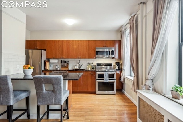 kitchen featuring sink, a breakfast bar, appliances with stainless steel finishes, backsplash, and light wood-type flooring