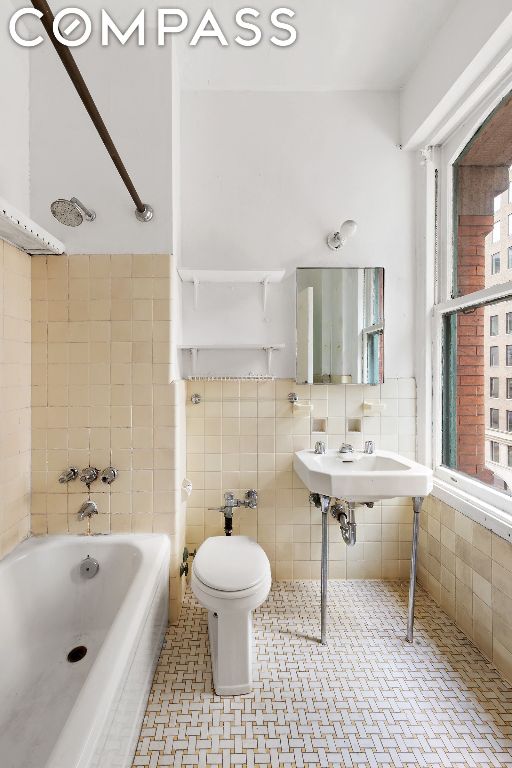 bathroom featuring tile patterned floors, toilet, sink, tile walls, and a bathing tub