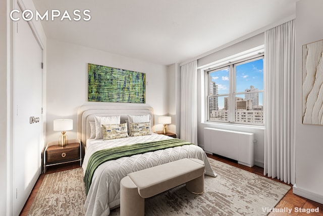 bedroom featuring a view of city, radiator, and wood finished floors