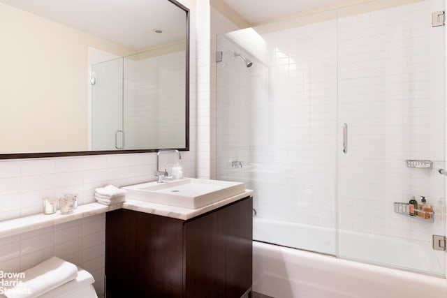 full bathroom with toilet, combined bath / shower with glass door, tile walls, and vanity