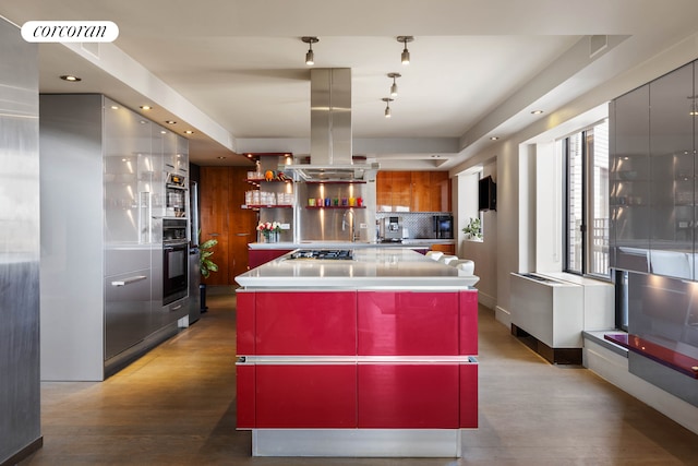 kitchen with black oven, red cabinets, decorative backsplash, island exhaust hood, and stainless steel gas stovetop