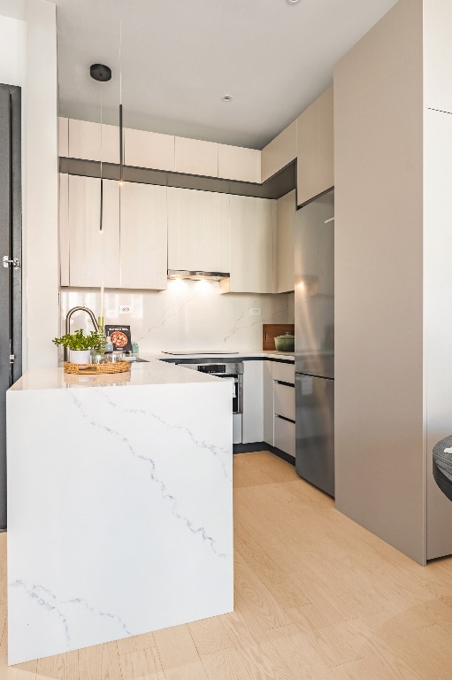 kitchen with decorative light fixtures, sink, stainless steel fridge, decorative backsplash, and light stone countertops