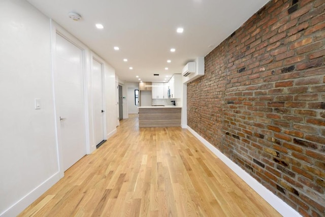 corridor with a wall mounted AC, brick wall, and light wood-type flooring