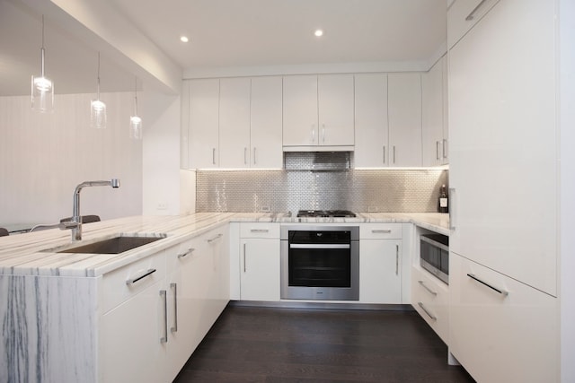 kitchen with backsplash, a sink, a peninsula, dark wood-style floors, and stainless steel appliances