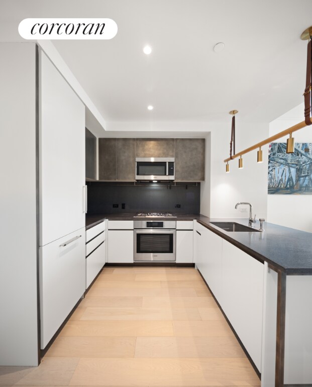 kitchen featuring sink, light hardwood / wood-style flooring, kitchen peninsula, stainless steel appliances, and white cabinets