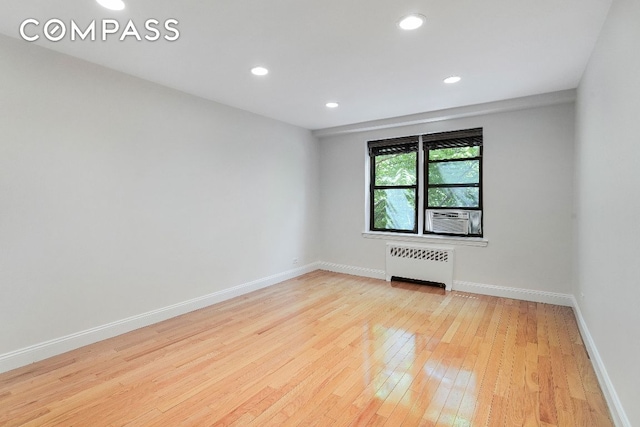 empty room with light wood-type flooring, cooling unit, and radiator heating unit