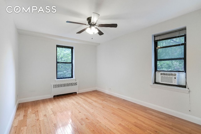 spare room featuring radiator, cooling unit, ceiling fan, and light hardwood / wood-style flooring